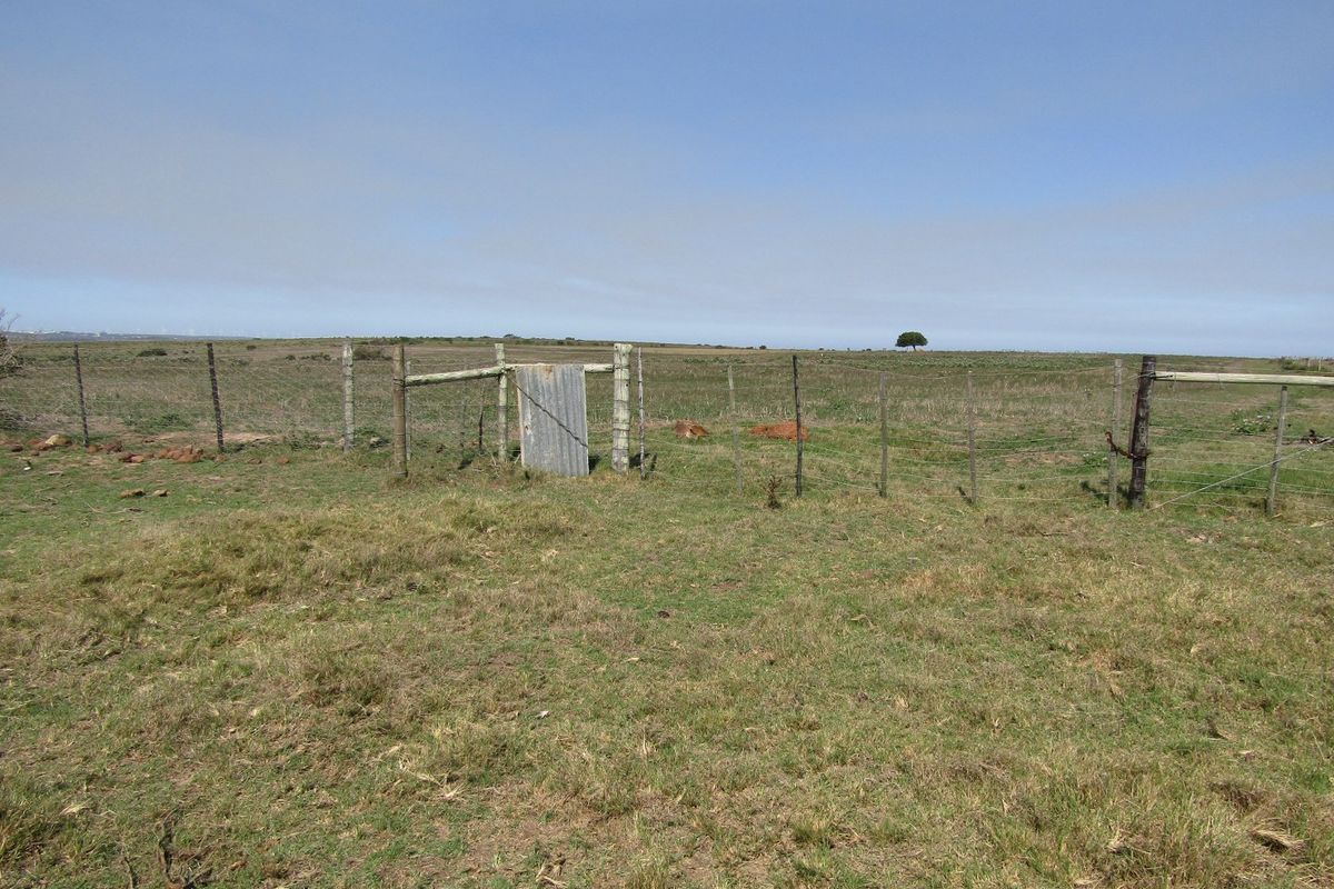 Expansive open farm land featuring wire perimeter fencing and a rustic corrugated metal gate.