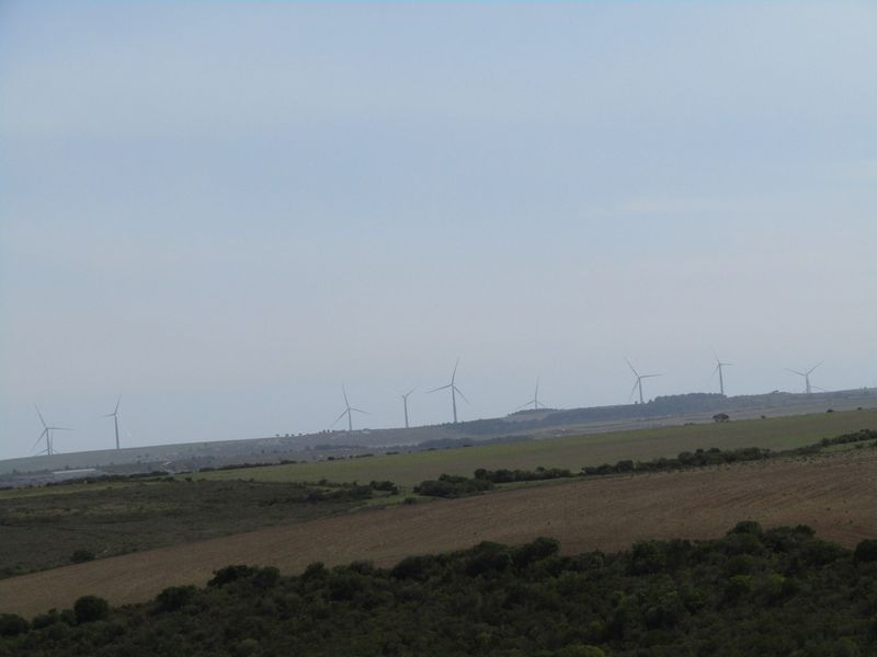 A wide landscape view of the farm property featuring rolling hills and distant wind turbines on the horizon.