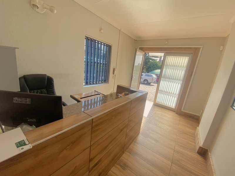 A professional commercial office reception area featuring a built-in wooden reception desk, tiled flooring, and a secure entrance door with a security gate.
