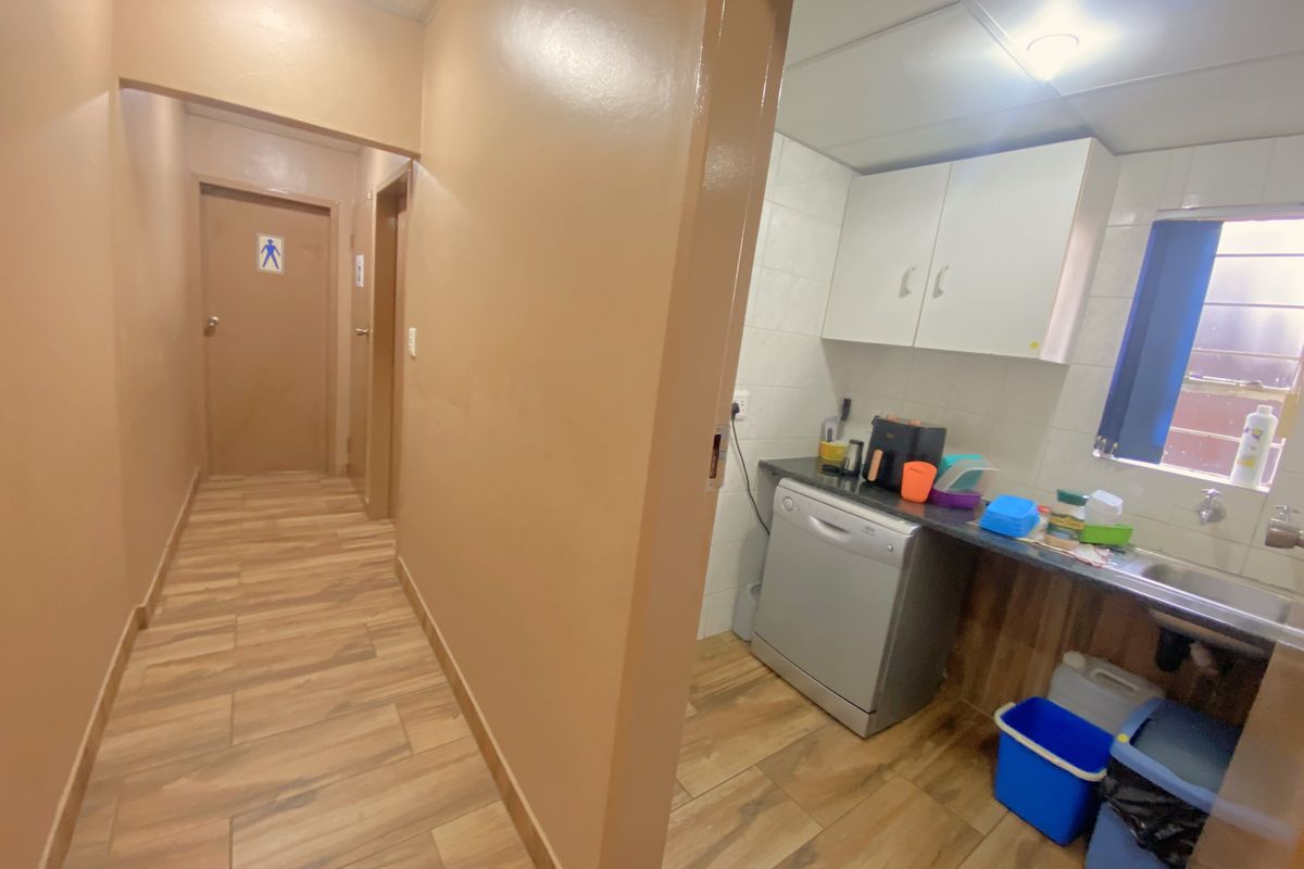 A functional kitchenette area featuring built-in cabinetry, a sink, and tiled flooring, adjacent to a hallway leading to restroom facilities.