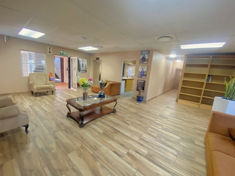 Spacious commercial reception or waiting area featuring wood-look tiled flooring, recessed ceiling lighting, and built-in shelving units.