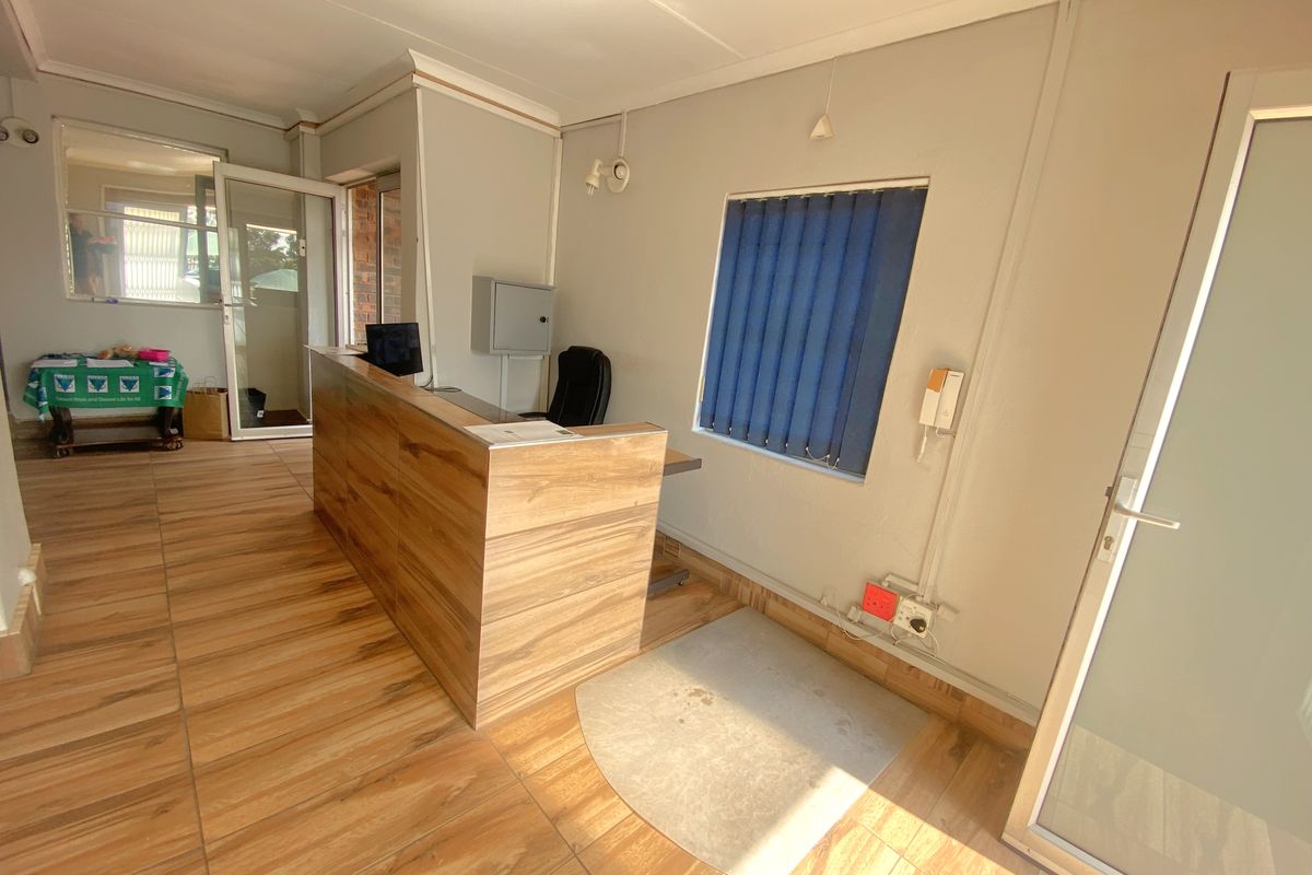 A functional commercial office space featuring wood-look tiled flooring, a built-in reception desk, and vertical window blinds.