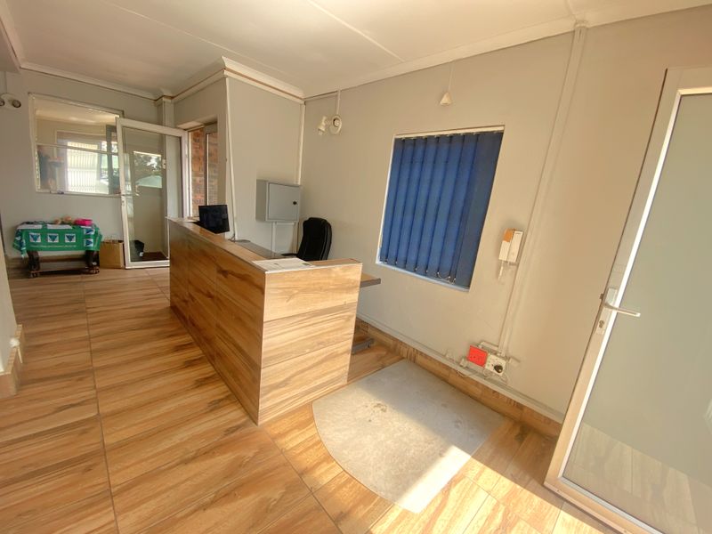 A functional commercial office space featuring wood-look tiled flooring, a built-in reception desk, and vertical window blinds.