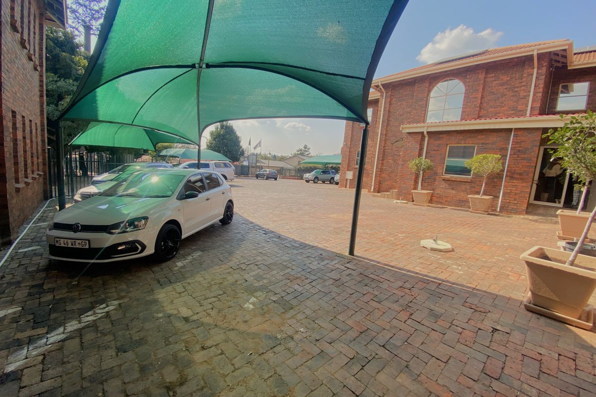 Commercial property exterior featuring a paved courtyard with shade-net covered parking bays and exposed brick building facades.