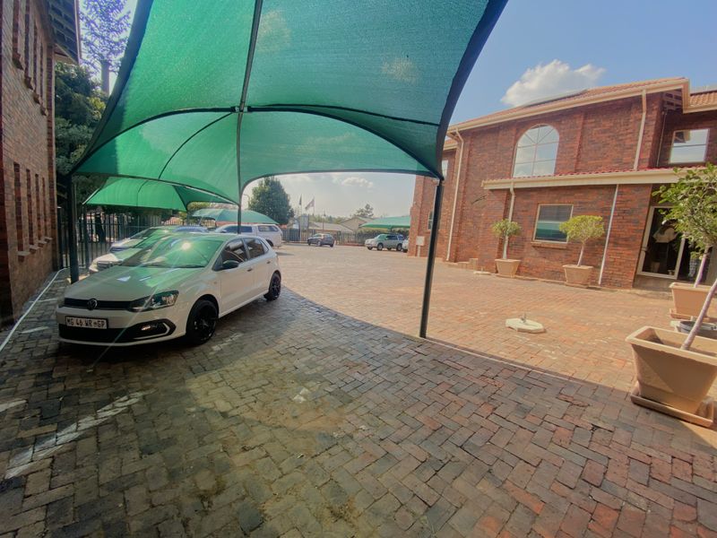 Commercial property exterior featuring a paved courtyard with shade-net covered parking bays and exposed brick building facades.