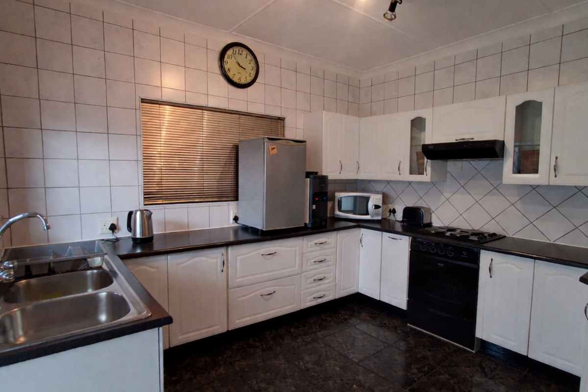 Functional kitchen featuring white cabinetry, dark laminate countertops, tiled walls, and integrated cooking appliances including an oven and extractor fan.