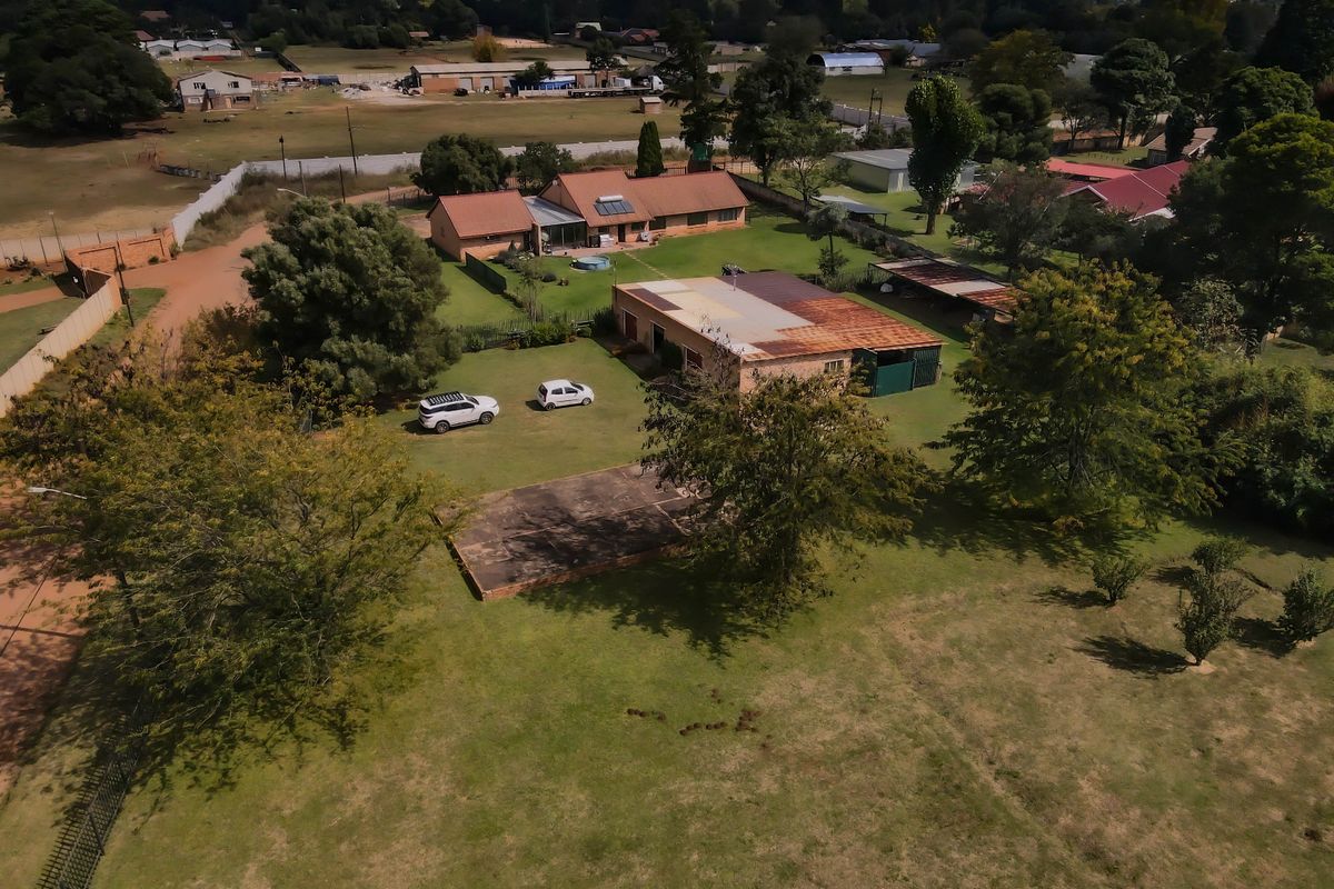 Aerial view of a small holding property featuring multiple structures, expansive garden space, and established trees in a rural setting.