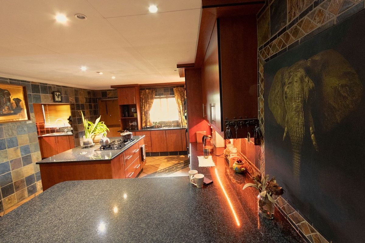 Spacious kitchen featuring dark wood cabinetry, granite countertops, a central island with a gas hob, and decorative tiled wall finishes.