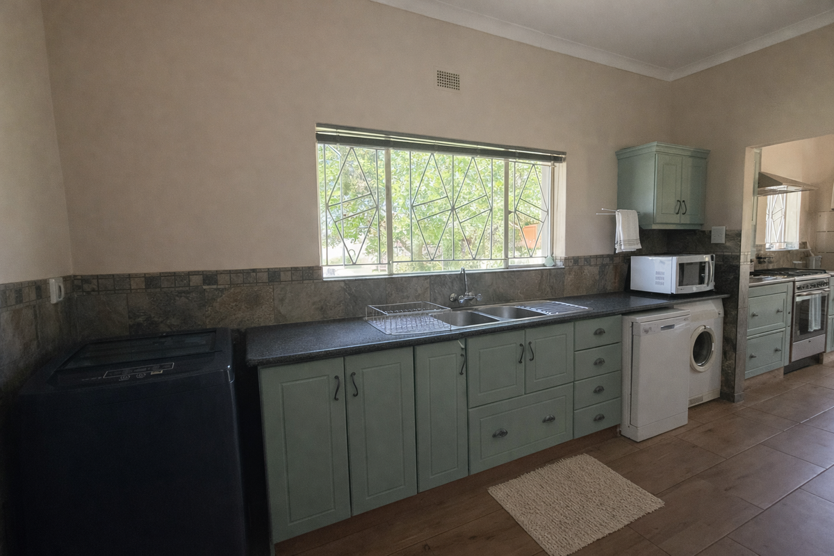 A functional kitchen featuring sage green cabinetry, stone countertops, a double basin sink, and tiled backsplash with security bars on the window.