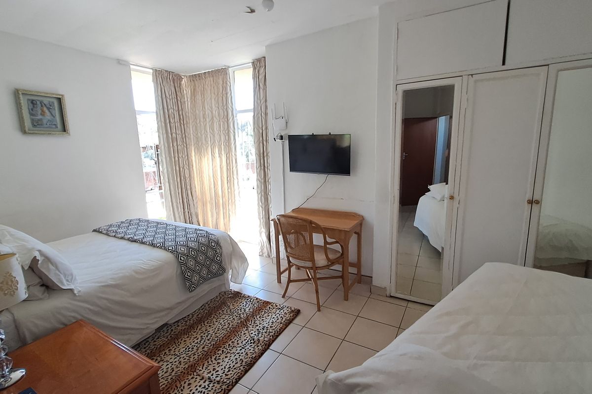 A functional hotel bedroom featuring tiled flooring, built-in mirrored wardrobes, and direct access to an outdoor area through sliding glass doors.
