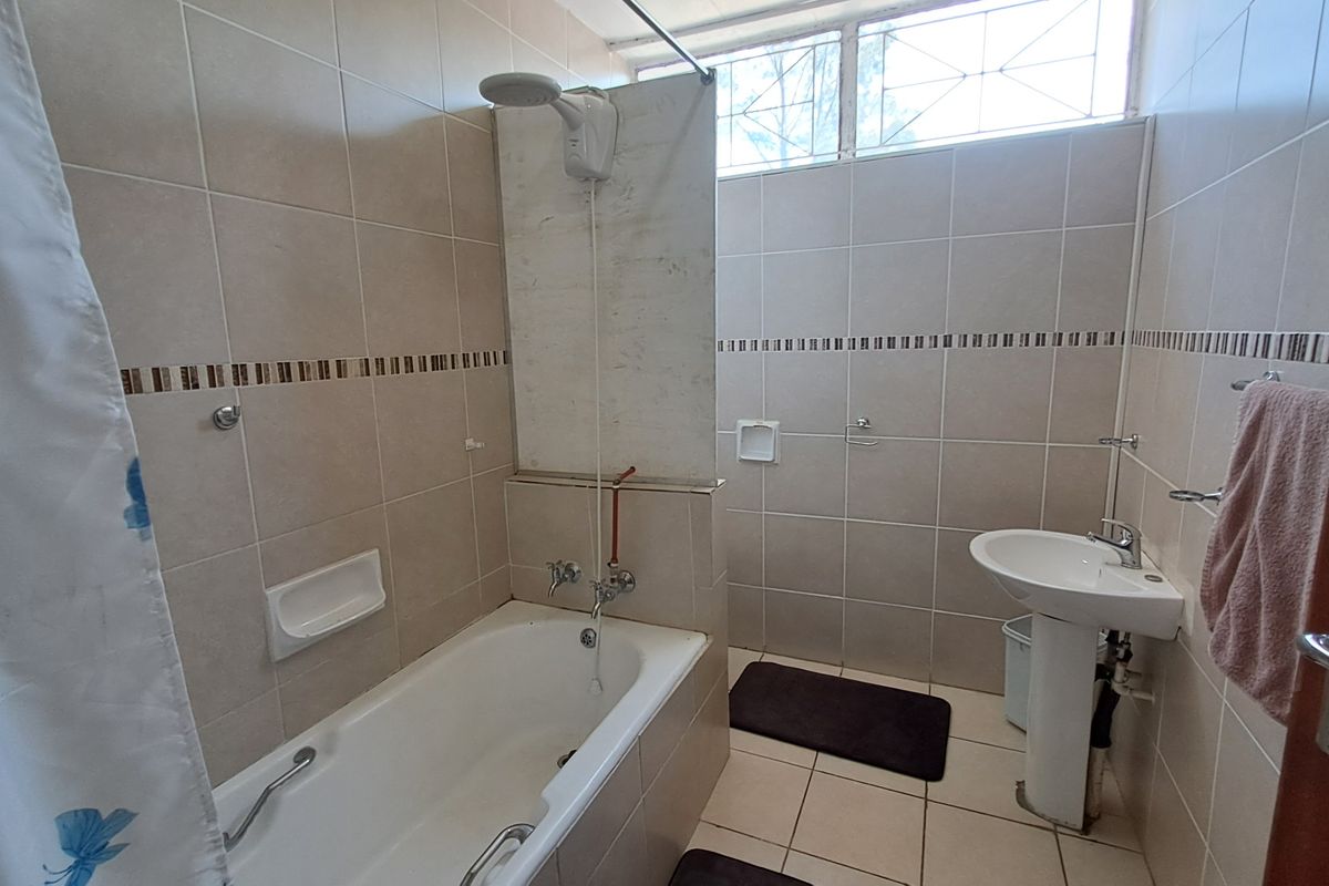 A functional bathroom featuring a bathtub with shower attachment, pedestal basin, and neutral ceramic wall and floor tiling.