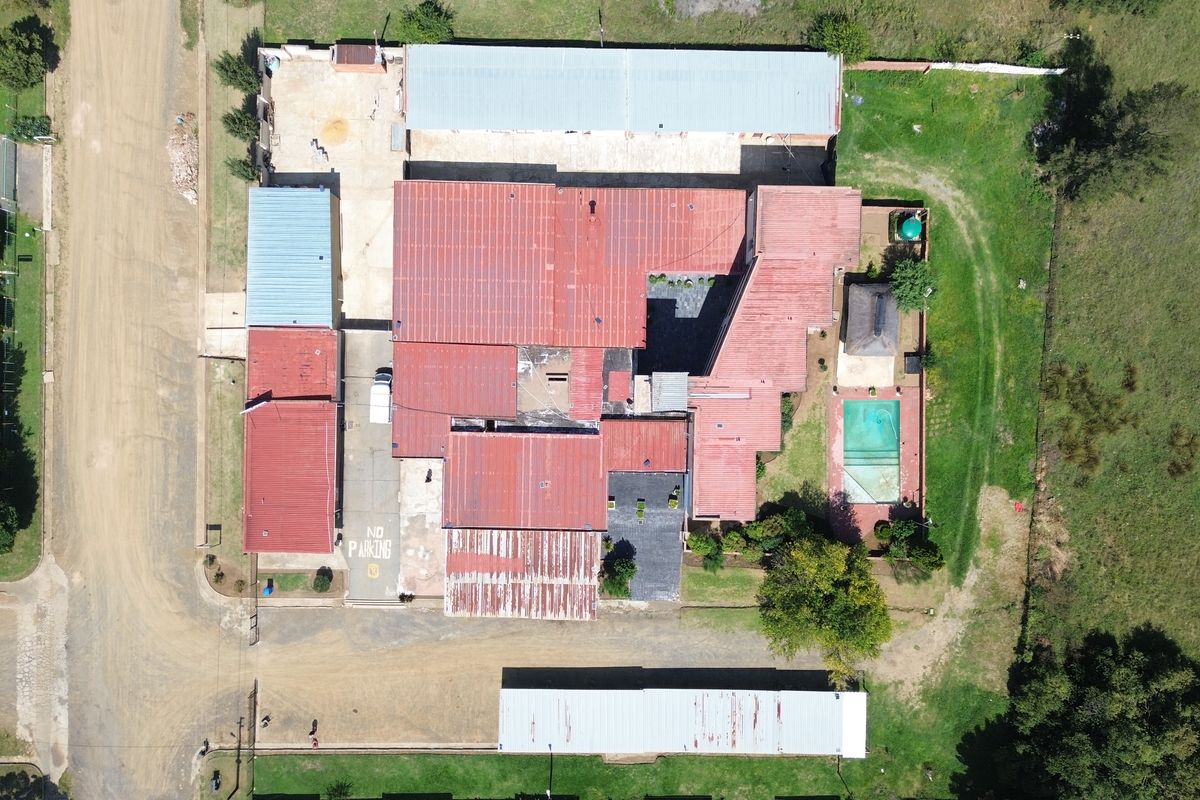 Aerial view of the hotel property featuring multiple buildings with metal roofing, a swimming pool, and paved parking areas.
