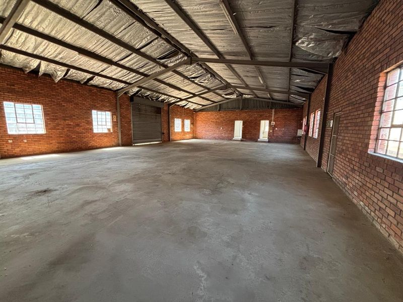Spacious industrial warehouse unit featuring exposed brick walls, concrete flooring, and high steel-truss ceilings with foil insulation, suitable for various commercial or storage uses.