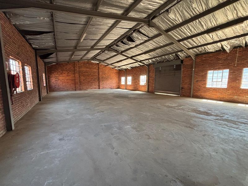 Spacious industrial warehouse unit featuring exposed brick walls, concrete flooring, a roller shutter door, and high-clearance steel frame construction.