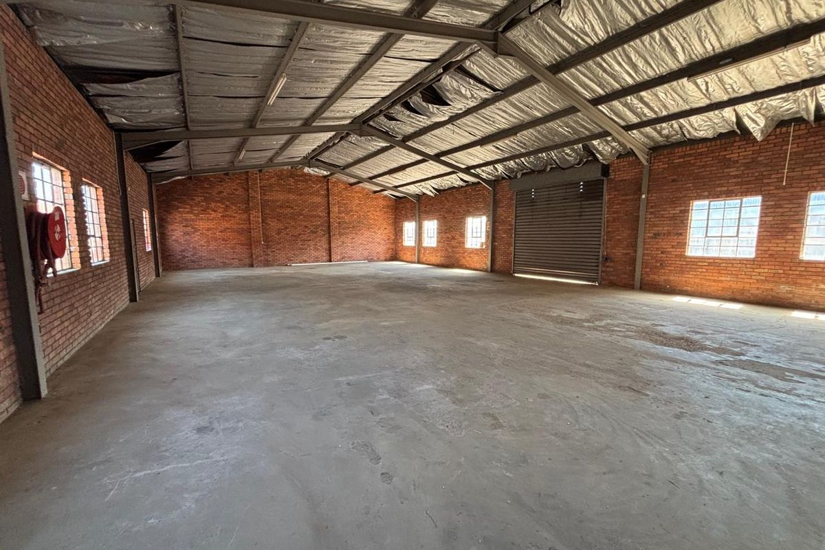 Spacious industrial warehouse unit featuring exposed brick walls, concrete flooring, a roller shutter door, and high-clearance steel frame construction.