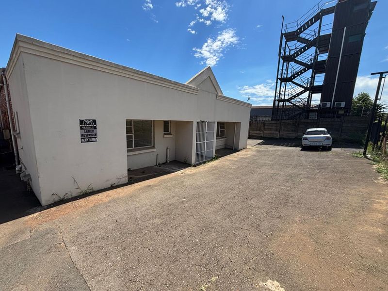 Rear exterior view of the industrial property featuring an asphalt yard, security gate, and external metal fire escape staircase.