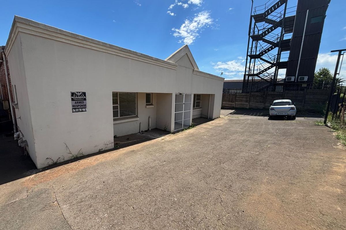 Rear exterior view of the industrial property featuring an asphalt yard, security gate, and external metal fire escape staircase.