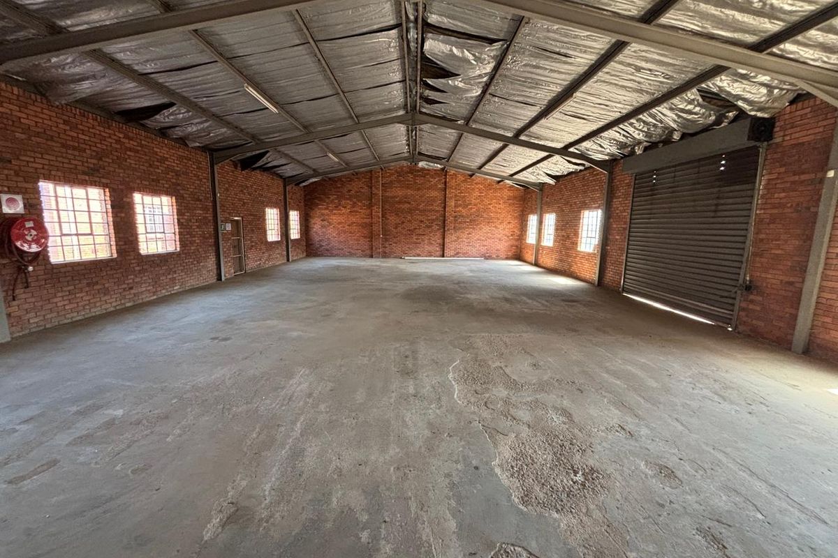 Spacious industrial warehouse unit featuring exposed brick walls, concrete flooring, steel roof trusses, and a large roller shutter door for easy access.
