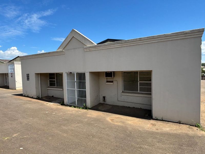 Front exterior view of an industrial unit featuring a paved driveway, security gate, and metal-framed windows.