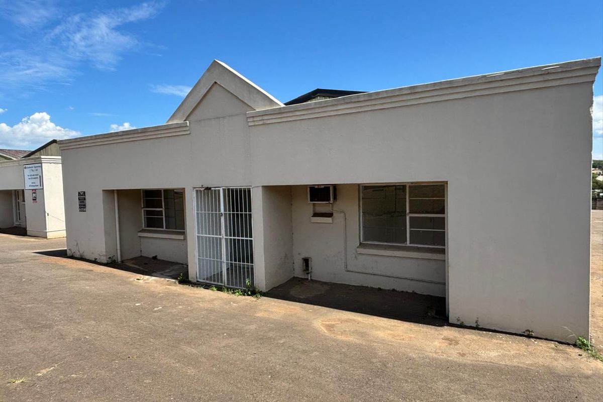 Front exterior view of an industrial unit featuring a paved driveway, security gate, and metal-framed windows.