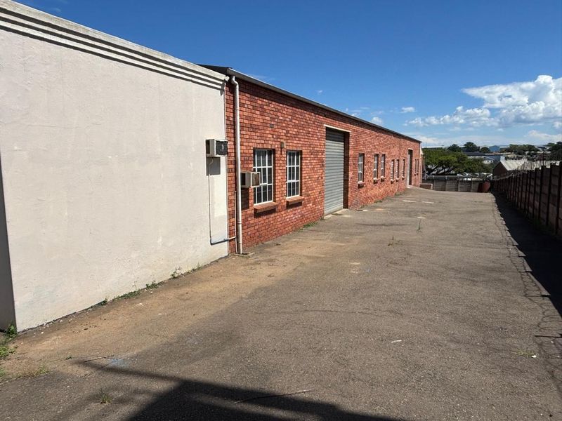 Rear industrial yard featuring a brick facade, roller shutter door access, and paved asphalt area with perimeter walling.