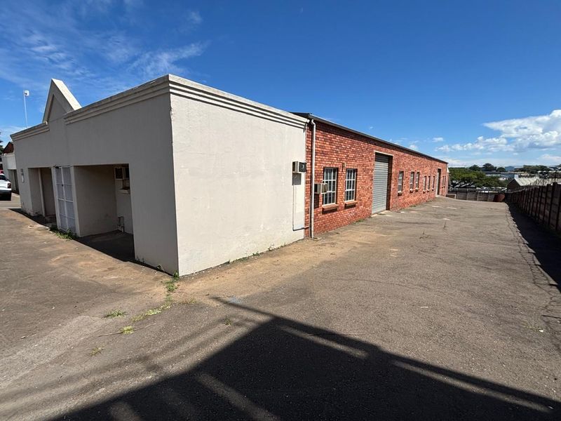 Rear exterior view of an industrial property featuring a brick facade, roller shutter door, and a large asphalt yard area.