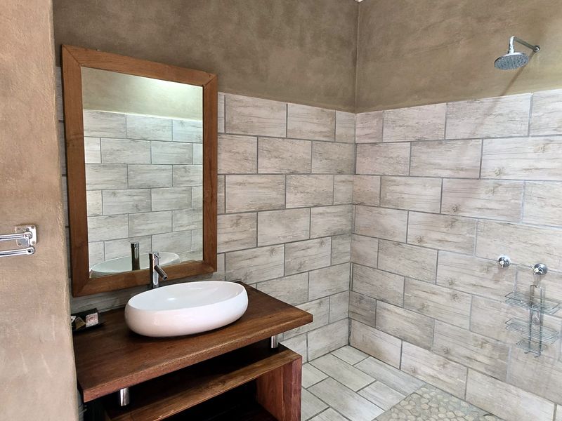 Modern bathroom featuring a vessel sink on a wooden vanity, tiled shower enclosure with a rainfall shower head, and neutral textured wall finishes.