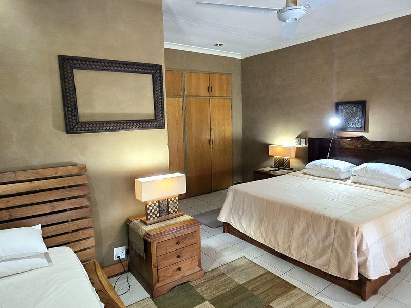 Spacious bedroom featuring built-in wooden cupboards, tiled flooring, and a ceiling fan, offering a comfortable and functional layout.