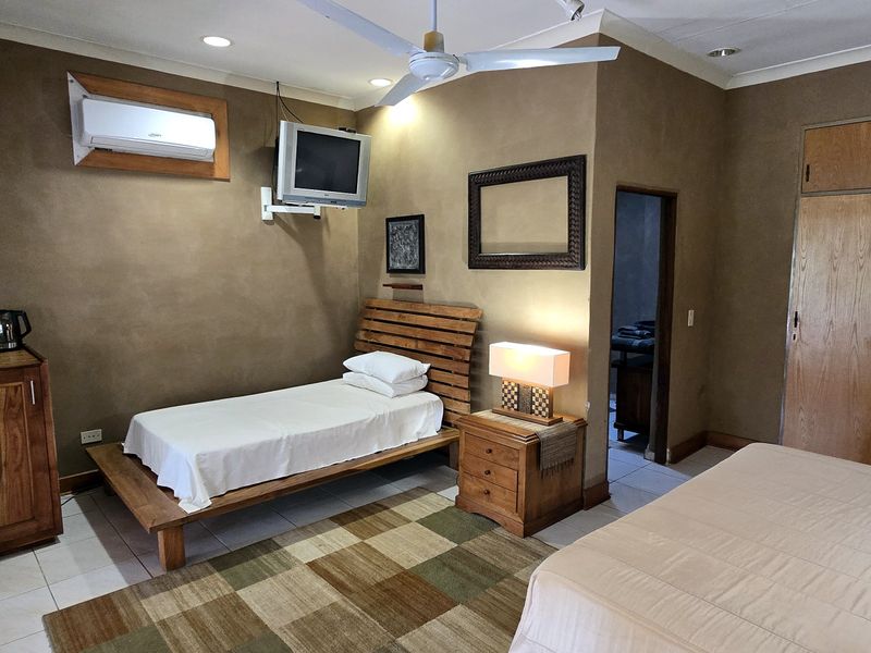 A bedroom featuring built-in wooden cupboards, tiled flooring, a ceiling fan, and a wall-mounted air conditioning unit.