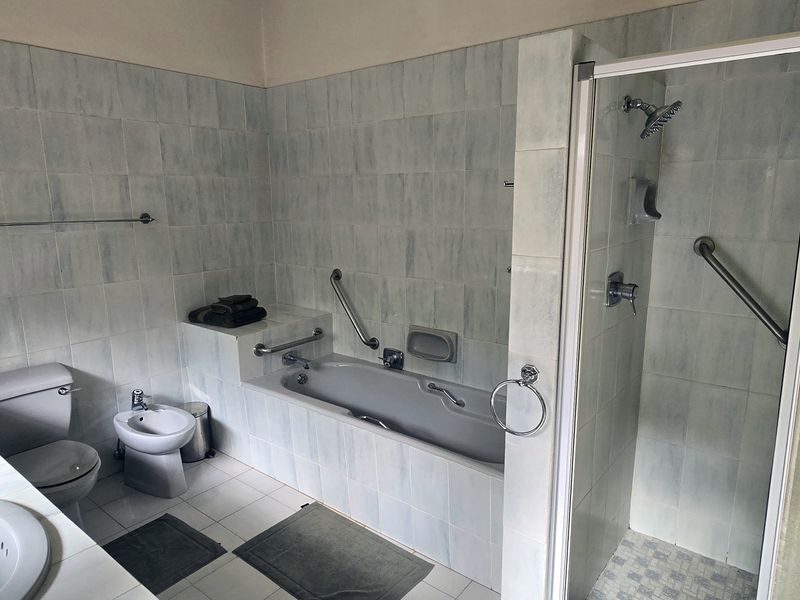 A spacious bathroom featuring a double vanity, built-in bathtub, separate shower enclosure, bidet, and toilet with installed safety grab rails.