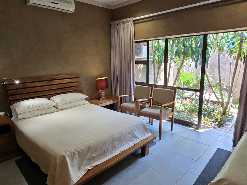 A well-maintained bedroom featuring tiled floors, an air conditioning unit, and a large sliding glass door providing direct access to a private garden area.