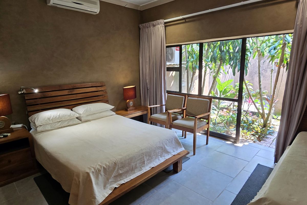 A well-maintained bedroom featuring tiled floors, an air conditioning unit, and a large sliding glass door providing direct access to a private garden area.