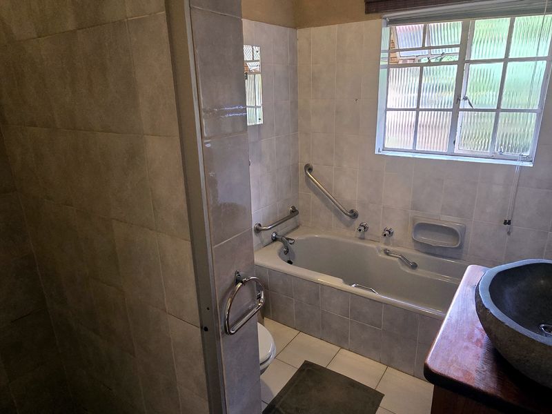 A functional bathroom featuring tiled walls and flooring, a bathtub with safety grab rails, and a stone-style basin.