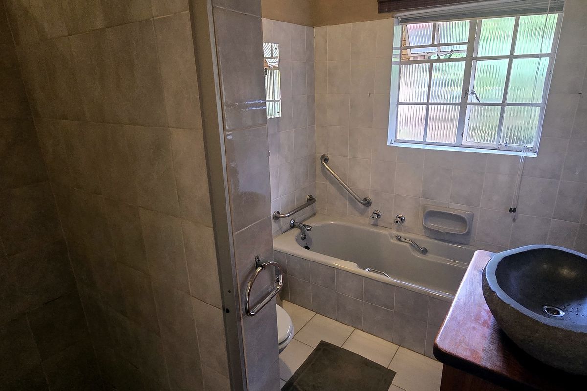 A functional bathroom featuring tiled walls and flooring, a bathtub with safety grab rails, and a stone-style basin.