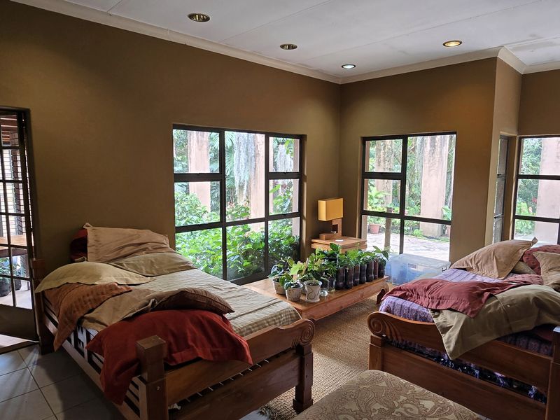 Spacious bedroom featuring large windows with garden views, tiled flooring, and recessed ceiling lighting, providing a bright and airy atmosphere.