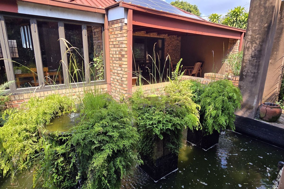 Rear exterior view featuring a covered patio, brick facade, and a built-in water feature with a pond.