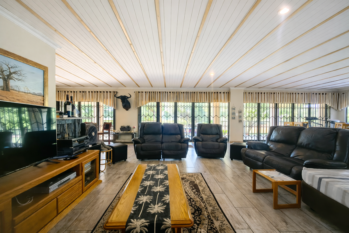 Spacious living room featuring tiled flooring, a unique timber-paneled ceiling, and large glass sliding doors with security gates providing ample natural light.