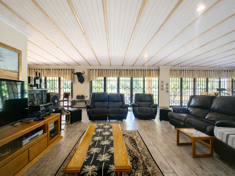 Spacious living room featuring tiled flooring, a unique timber-paneled ceiling, and large glass sliding doors with security gates providing ample natural light.