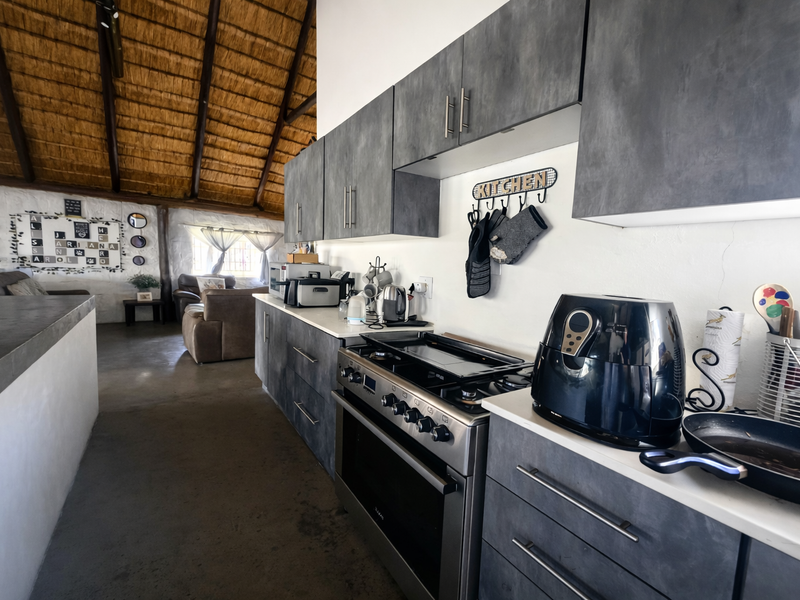 Open-plan kitchen area featuring modern dark cabinetry, a gas stove, and a distinctive high-pitched thatched roof with exposed timber rafters.