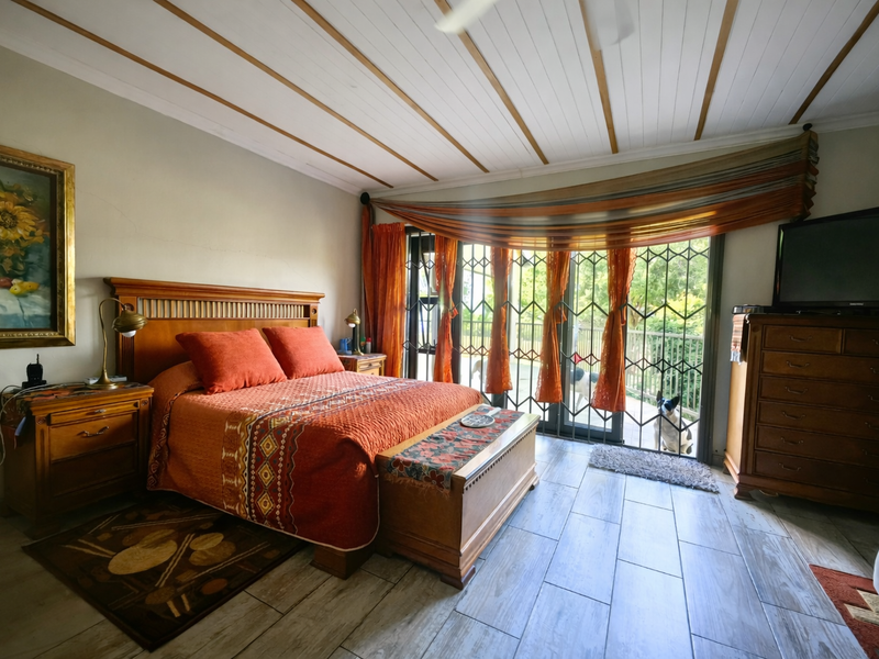 A spacious bedroom featuring wood-look tile flooring, an exposed beam ceiling, and a sliding glass door with security gate leading to the outdoors.