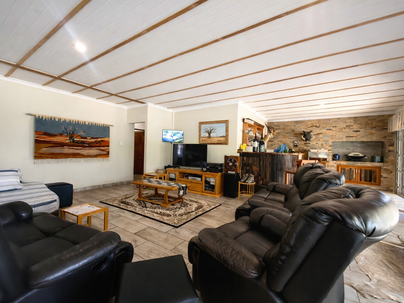 Spacious open-plan living area featuring a stone accent wall, built-in bar, tiled flooring, and a distinctive timber panelled ceiling.