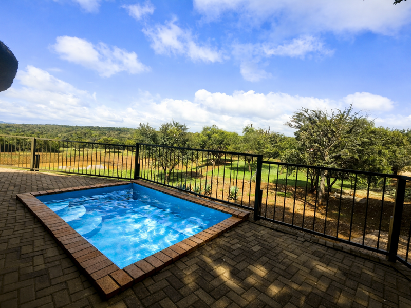 A compact plunge pool set within a paved patio area, featuring metal safety railings and expansive views of the surrounding farm landscape.