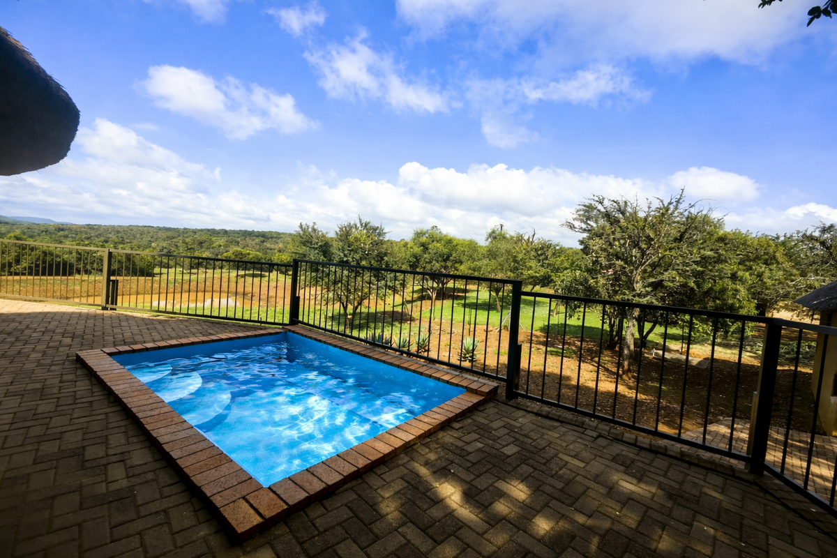 A compact plunge pool set within a paved patio area, featuring metal safety railings and expansive views of the surrounding farm landscape.