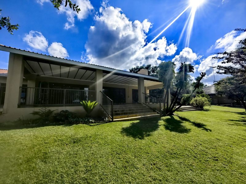 A spacious rear exterior view of the farm property featuring a large covered patio, metal railings, and well-maintained garden grounds.