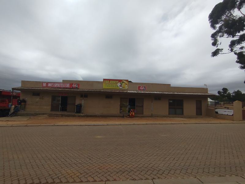 Single-story commercial building featuring a paved frontage, multiple entrance points with security gates, and prominent signage for a superette and fisheries business.