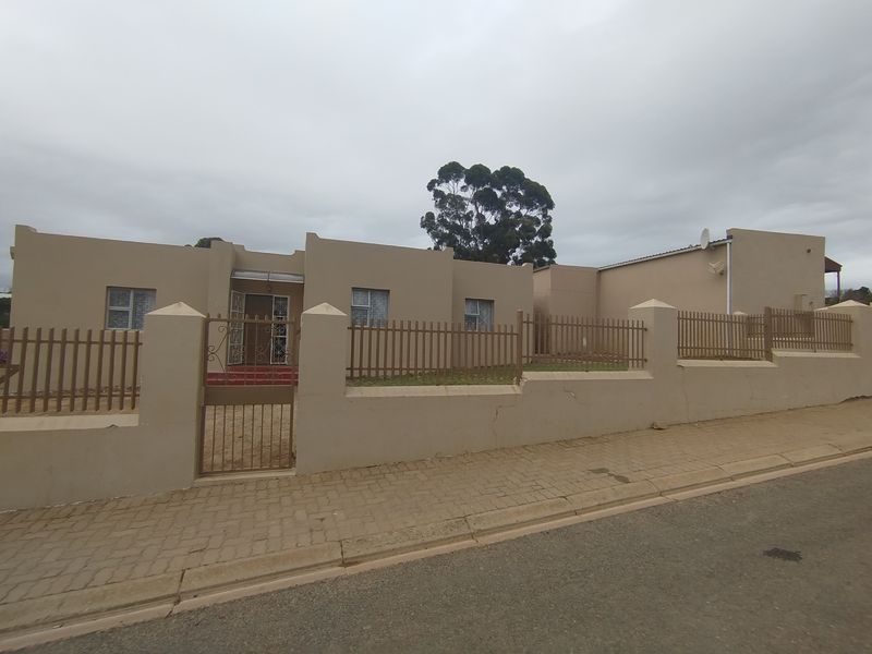 Front exterior view of a single-story building featuring a perimeter wall with metal fencing and a pedestrian gate, situated along a paved street.