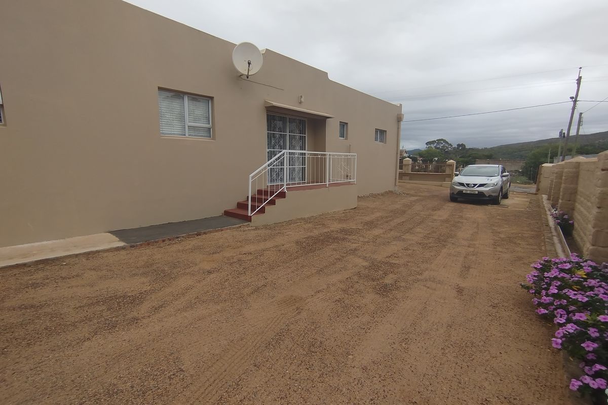 Rear exterior view of the property featuring a beige facade, security gate with stairs, and an unpaved driveway area.