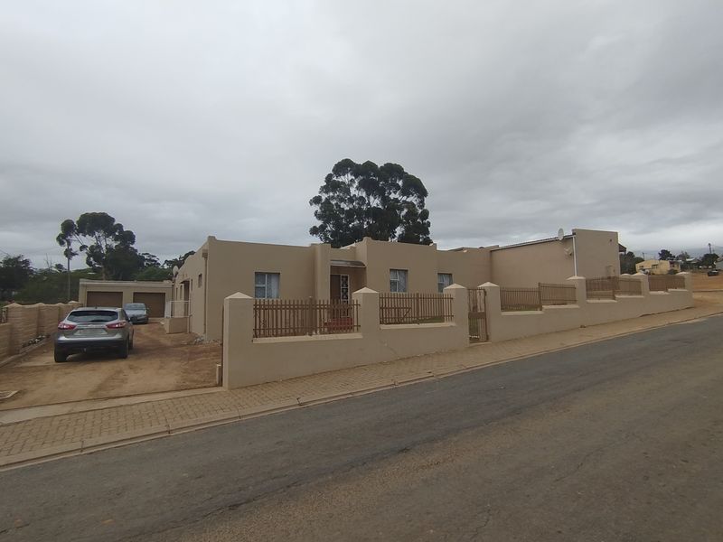 Front exterior view of a single-story property featuring a perimeter wall, metal fencing, and a paved driveway leading to a double garage.