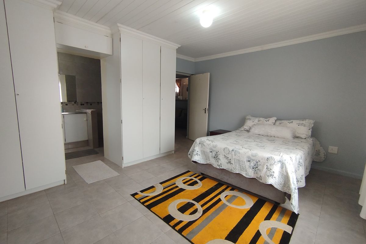 Spacious bedroom featuring built-in cupboards, tiled flooring, and a tongue and groove ceiling, with convenient access to an en-suite bathroom.