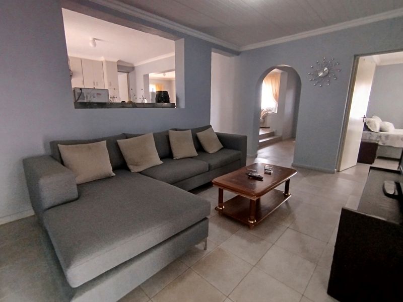 A living room featuring tiled flooring, a coved ceiling, and an arched doorway leading to adjacent spaces, with a pass-through window to the kitchen.